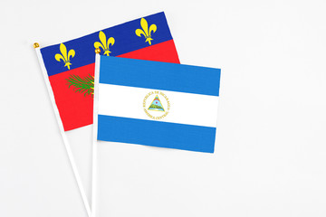 Nicaragua and Guadeloupe stick flags on white background. High quality fabric, miniature national flag. Peaceful global concept.White floor for copy space.
