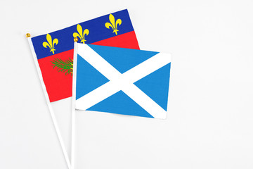Scotland and Guadeloupe stick flags on white background. High quality fabric, miniature national flag. Peaceful global concept.White floor for copy space.