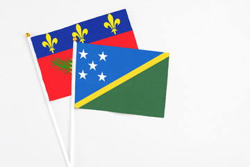 Solomon Islands and Guadeloupe stick flags on white background. High quality fabric, miniature national flag. Peaceful global concept.White floor for copy space.