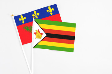 Zimbabwe and Guadeloupe stick flags on white background. High quality fabric, miniature national flag. Peaceful global concept.White floor for copy space.