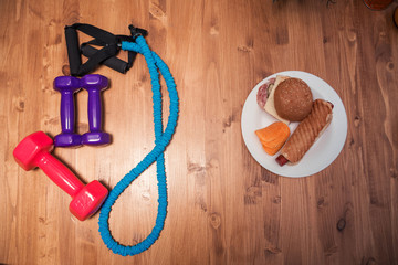 Sports equipment and plate with fast food on a wooden background. The choice between sports and fast food
