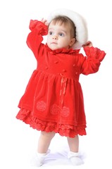 Cute standing one year old little girl poses in fur cap. Christmas children clothes. Funny toddler in red dress on white isolated background