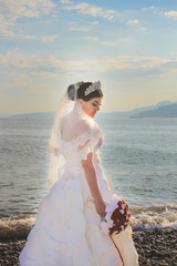 Fototapeta na wymiar Wedding by the sea. Bride with a red bouquet. Mountains and sea background. Adorable bride. Sunrise view. Concept marriage, just married.