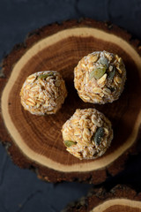 Vegan food concept. Close up of frozen oatmeal energy balls with pumpkin seeds on oak wood slab on black background top view