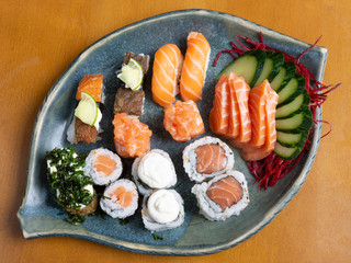 Sushi, sashimi, rolls and vegetables on a leaf shaped dish over wooden table. Japanese food.