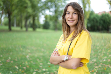 Mujer enfermera joven y sonriente con uniforme amarillo y estetoscopio con los brazos cruzados en entorno natural