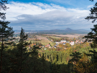 Fototapeta na wymiar View from Hrabencina vyhlidka lookout on village Sloup v cechach in luzicke hory, Lusatian Mountains with autumn colored deciduous and coniferous tree forest and green hills, blue sky, white clouds