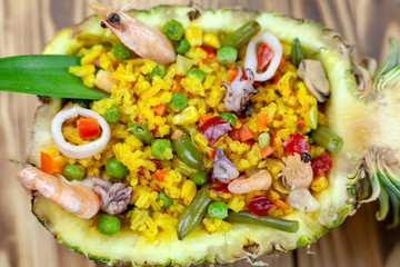 Rice in a pineapple with seafood on a wooden background, close-up