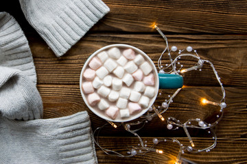 Tasty hot chocolate and beige wolleen sweater on rustic brown table, close up, top view. Cozy winter evening. 