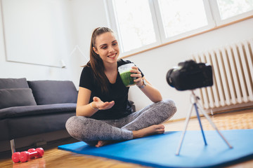 young woman fitness vlogger in her home, drinking healthy green smoothie