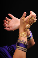 Female hands in massive jewelry as golden bracelet and rings. Movement of national indian dance. Isolated on dark background