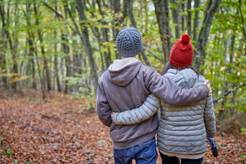 Fototapeta premium a couple with their backs embraced walking through the forest in autumn, colors orange brown, green, yellow