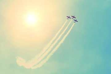 Group of three turboprop aircraft flying in the sky sun shine leaving a white smoky trail.