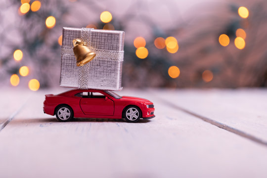 Miniature Red Car Carrying a big silver box on colorful bokeh background. Holiday Merry Christmas concept
