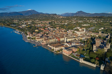 Fototapeta na wymiar Aerial view of Lake Garda and the city center of Lazise, Italy. Autumn season, blue sky, Monte Baldo on the horizon, snow in the mountains