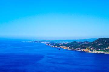 Fototapeta na wymiar Blue sea, clear cloudless sky and shore with green hills, top view.