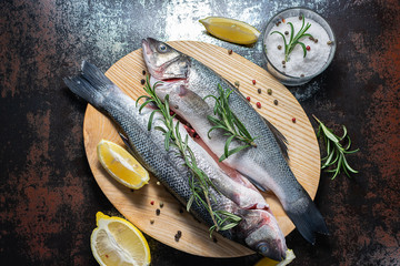 Fresh raw wild sea bass with herbs and spices on wooden cutting board top view. Healthy and organic food concept. Seafood concept.