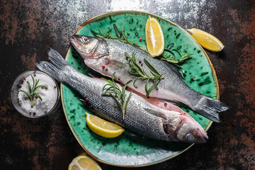Fresh organic sea bass with lemons, herbs and spices on dark kitchen table top view. Healthy and organic food concept.