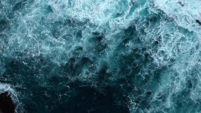 Aerial top down shot of stormy waves in Atlantic ocean breaking at black rocks. Shot in cloudy rainy weather with huge wind.