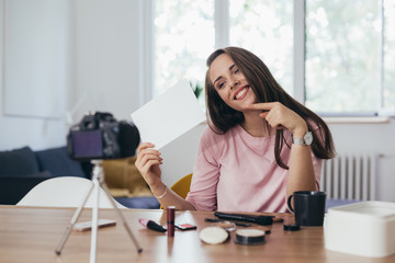 woman makeup vlogger at her home, holding blank cardboard