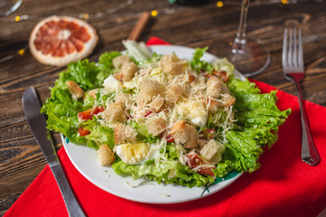 Christmas table with appetizing green Caesar salad with lettuce leaves and a glass on a red napkin on a wooden table
