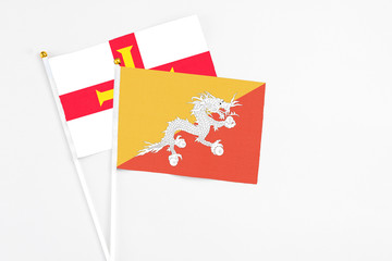 Bhutan and Guernsey stick flags on white background. High quality fabric, miniature national flag. Peaceful global concept.White floor for copy space.