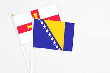 Bosnia Herzegovina and Guernsey stick flags on white background. High quality fabric, miniature national flag. Peaceful global concept.White floor for copy space.