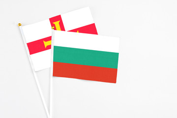 Bulgaria and Guernsey stick flags on white background. High quality fabric, miniature national flag. Peaceful global concept.White floor for copy space.