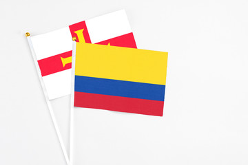 Colombia and Guernsey stick flags on white background. High quality fabric, miniature national flag. Peaceful global concept.White floor for copy space.