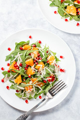 Fresh green organic salad with raw ingredients close up. Tasty salad with arugula, orange slices, pomegranate and cheese on white plate, top view. Healthy eating, dieting concept