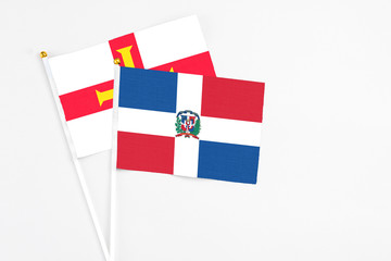 Dominican Republic and Guernsey stick flags on white background. High quality fabric, miniature national flag. Peaceful global concept.White floor for copy space.