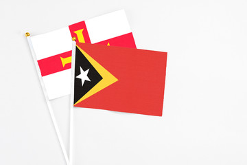 East Timor and Guernsey stick flags on white background. High quality fabric, miniature national flag. Peaceful global concept.White floor for copy space.