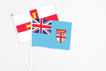 Fototapeta premium Fiji and Guernsey stick flags on white background. High quality fabric, miniature national flag. Peaceful global concept.White floor for copy space.