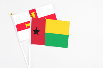 Guinea Bissau and Guernsey stick flags on white background. High quality fabric, miniature national flag. Peaceful global concept.White floor for copy space.