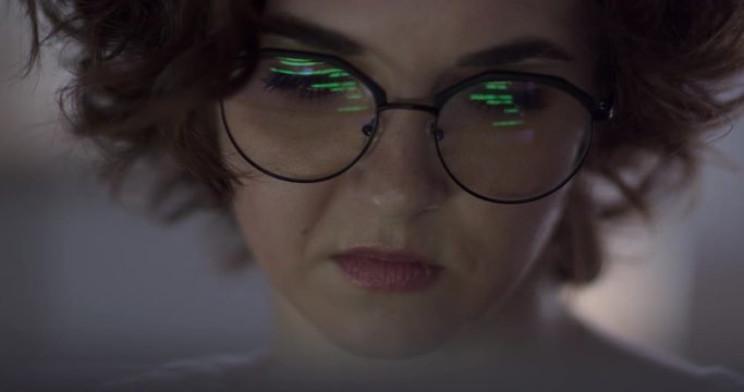 Hacker Woman Tries to Get Confidential Information. Pretty hacker woman attacks confidational data using programme code. We see the reflection of the code in her glasses