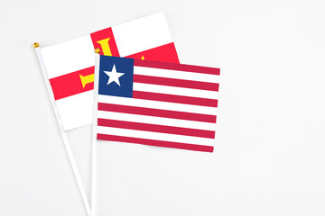 Liberia and Guernsey stick flags on white background. High quality fabric, miniature national flag. Peaceful global concept.White floor for copy space.