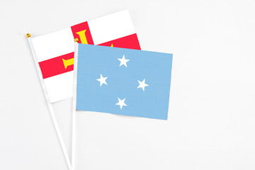 Micronesia and Guernsey stick flags on white background. High quality fabric, miniature national flag. Peaceful global concept.White floor for copy space.