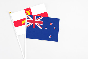 Fototapeta premium New Zealand and Guernsey stick flags on white background. High quality fabric, miniature national flag. Peaceful global concept.White floor for copy space.