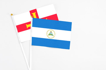 Nicaragua and Guernsey stick flags on white background. High quality fabric, miniature national flag. Peaceful global concept.White floor for copy space.