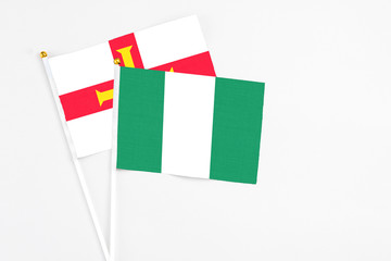 Fototapeta premium Nigeria and Guernsey stick flags on white background. High quality fabric, miniature national flag. Peaceful global concept.White floor for copy space.