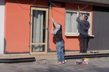 Two men paint the wall orange on the street with cushions.