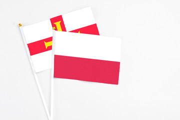 Poland and Guernsey stick flags on white background. High quality fabric, miniature national flag. Peaceful global concept.White floor for copy space.