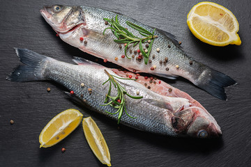 Raw wild sea bass with herbs and spices on black stone background top view. Healthy and organic food concept.