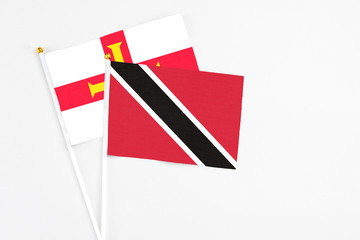 Trinidad And Tobago and Guernsey stick flags on white background. High quality fabric, miniature national flag. Peaceful global concept.White floor for copy space.