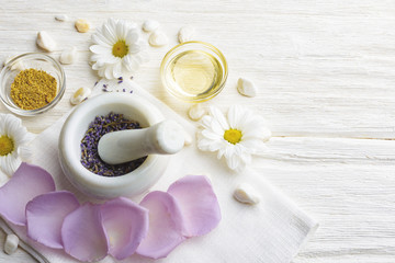 Obraz na płótnie Canvas Composition with dried lavender flowers in white marble pestle and mortar and natural chamomile oil cosmetic in glass jar on white background, top view with free copy space