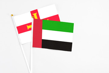 United Arab Emirates and Guernsey stick flags on white background. High quality fabric, miniature national flag. Peaceful global concept.White floor for copy space.