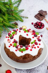 Fototapeta na wymiar Chocolate cake Christmas wreath with sugar icing, cranberries, pomegranate and mint leaves on top. Festive Dessert for Christmas and New Year.