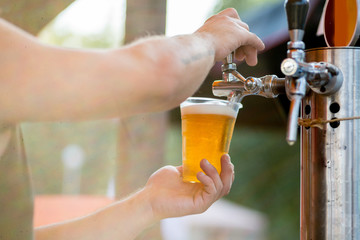beer is poured into a glass from a tap. The bartender pours beer into a plastic glass - 302751534