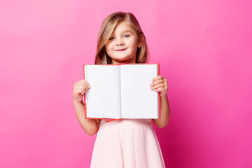 Pretty smiling girl in pink dress holding book with empty pages for your text - obrazy, fototapety, plakaty