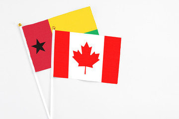 Fototapeta na wymiar Canada and Guinea Bissau stick flags on white background. High quality fabric, miniature national flag. Peaceful global concept.White floor for copy space.